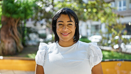 Smiling hispanic woman in park with greenery