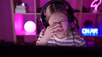 Young stressed woman with headset in a dark gamer room feeling tired or having a headache