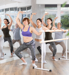 Group of beginners women rehearsing plie ballet movement at barre in dance studio