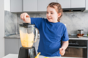 Pretty little girl making fruit puree in a blender at home in the kitchen. Selected focus.