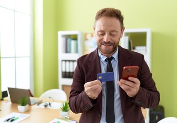 Middle age man business worker using smartphone and credit card at office