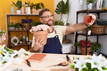 Middle age man florist make selfie by smartphone holding plant at flower shop