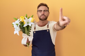 Middle age man with beard florist shop holding flowers pointing with finger up and angry expression, showing no gesture