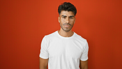 Young hispanic adult man with a beard posing in a white shirt against a red isolated background,...