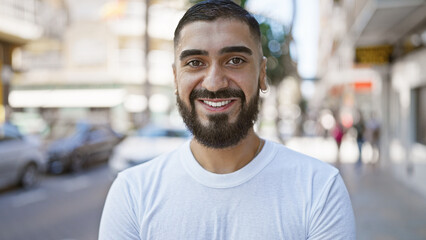 A cheerful young man with a beard smiles on a sunny city street, portraying urban lifestyle and positivity.