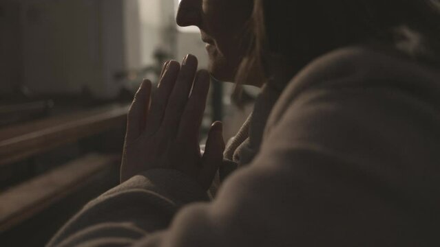 Folded arms of religious woman praying in Christian church close up. Mid adult female sitting with closed eyes during prayer in cathedral side view. Catholicism concept