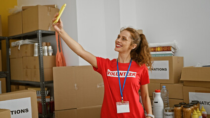 A cheerful caucasian woman volunteer takes a selfie in a storeroom filled with donation boxes