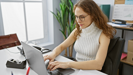A focused young hispanic woman working on a laptop in a modern office setting, showcasing...