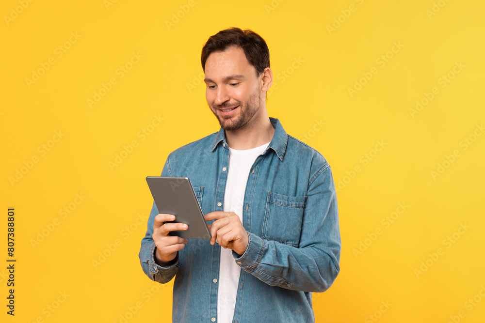 Poster guy wearing a blue shirt is engrossed in using a tablet device. he is focused on the screen, possibl