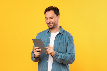 Guy wearing a blue shirt is engrossed in using a tablet device. He is focused on the screen,...