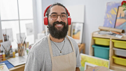 A cheerful hispanic man with a beard and headphones in an art studio.