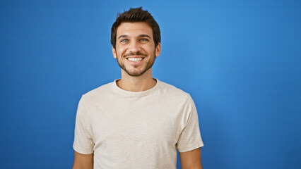 Handsome young hispanic man with a beard smiling confidently against a solid blue background.