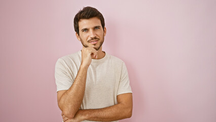 Handsome young hispanic man with beard posing thoughtfully against a pink wall.