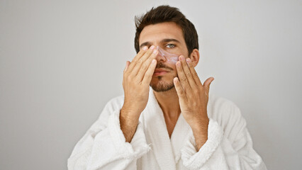 Handsome hispanic man applying facial skincare treatment against a white background