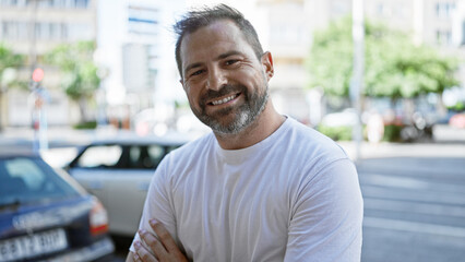 Fototapeta premium Handsome mature hispanic man with grey hair smiling outdoors in an urban city setting.