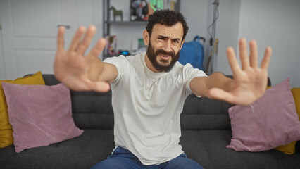 Bearded man gestures stop in a modern living room setting, evoking themes of rejection or...