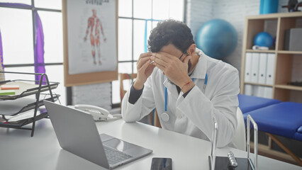 Stressed male doctor with beard holding head in hands at clinic office