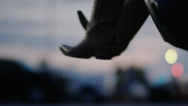 Woman wearing cowboy boots swings her feet while sitting in the trunk of a car during a tailgate