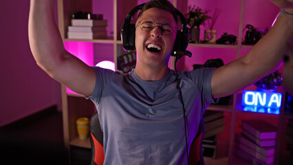 A joyful hispanic man celebrating a victory in a gaming room with neon lights at night.