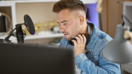 Focused hispanic man with headphones in music studio near microphone and instruments