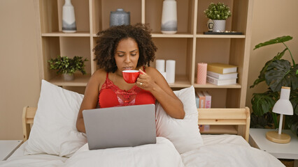 African american woman with braids using laptop and drinking coffee in bedroom