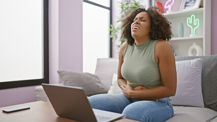 African american woman with pain sitting on a couch with a laptop