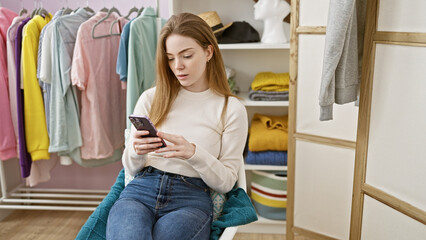 A young blonde woman casually dressed, browses her phone in a modern dressing room surrounded by...