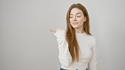 A smiling young caucasian woman with blonde hair, wearing a white sweater, gestures with her thumb...