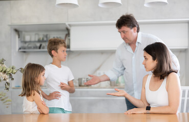 Irate parents abusing preteen son and little daughter standing by the table in the kitchen