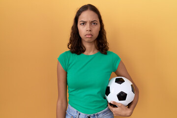 Young hispanic woman holding ball skeptic and nervous, frowning upset because of problem. negative...