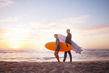Surf enthusiasts, a man and teenager, in wetsuits hold boards