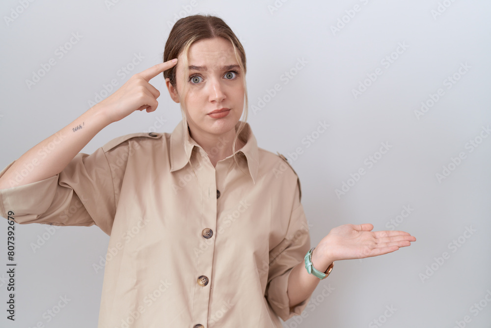 Sticker Young caucasian woman wearing casual shirt confused and annoyed with open palm showing copy space and pointing finger to forehead. think about it.