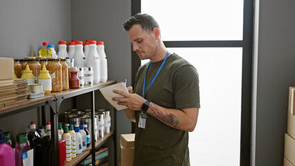 Hispanic man with tattoo and badge writing inventory in storeroom among shelves with supplies
