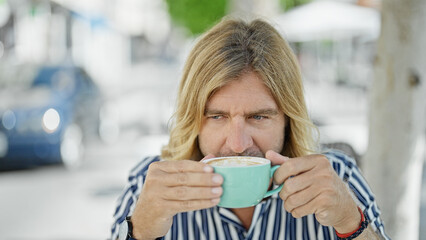 A handsome man with long blond hair enjoying a coffee at an outdoor urban cafe