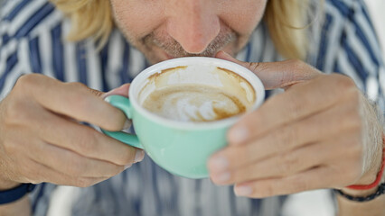 Handsome young man with long blond hair enjoying a cappuccino at an outdoor cafe