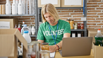 Blond man volunteering organizing donations in a warehouse checks information on a laptop.