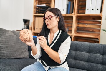 Young beautiful hispanic woman psychologist pointing with finger to brain at psychology clinic
