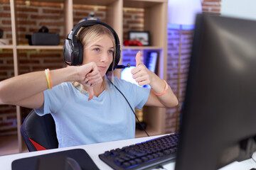 Young caucasian woman playing video games wearing headphones doing thumbs up and down, disagreement and agreement expression. crazy conflict