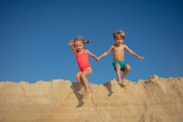 Happy siblings take playful leap from a sand heap on sunlit day