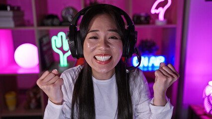 Excited young asian woman celebrating success in a colorful gaming room with neon lights at night.