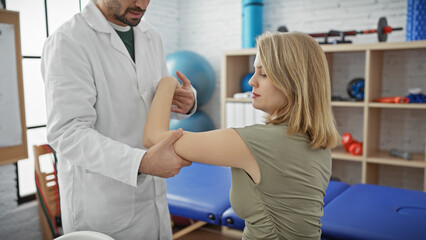 Obraz premium A man, possibly a physiotherapist, assists a woman with an arm exercise in a professional indoor therapy clinic.