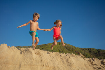 Two cheerful kids are engaging in playful jump from sandy dune