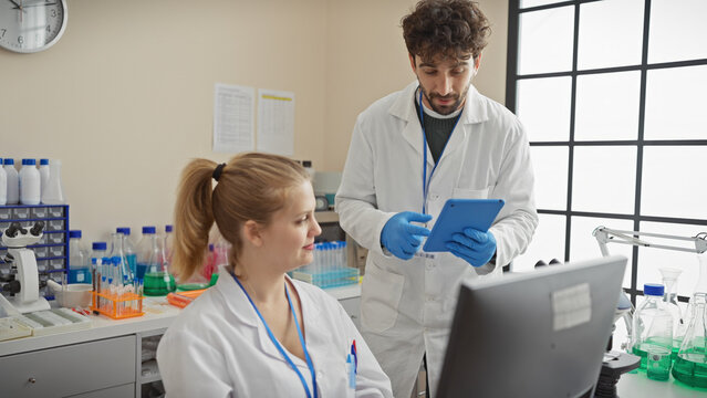A man and woman in lab coats work together in a laboratory, using technology and science equipment.