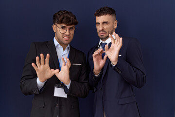 Two hispanic business men wearing business clothes disgusted expression, displeased and fearful doing disgust face because aversion reaction. with hands raised