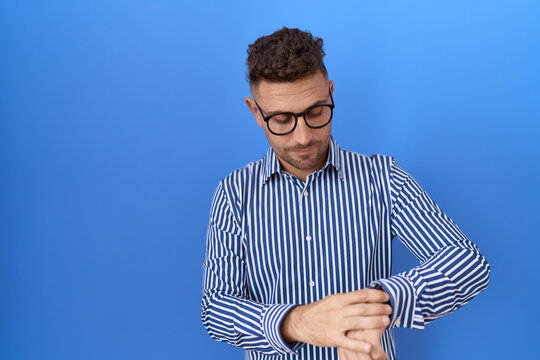 Hispanic man with beard wearing glasses checking the time on wrist watch, relaxed and confident