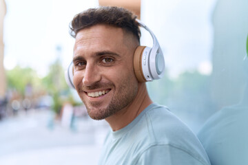 Young hispanic man listening to music standing at street