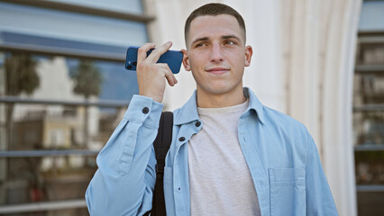 A young hispanic man listens to a voicemail outdoors in a casual urban setting.