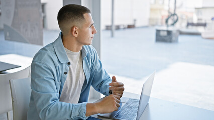 A young hispanic man using a laptop in a brightly lit modern university interior, embodying a...