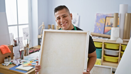 Smiling confident young latin man artist, joyfully holding his drawing, standing in the heart of...