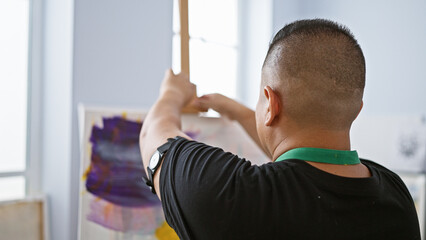 Passionate young latin artist, brush in hand, sets up his canvas to draw on an easel inside his...